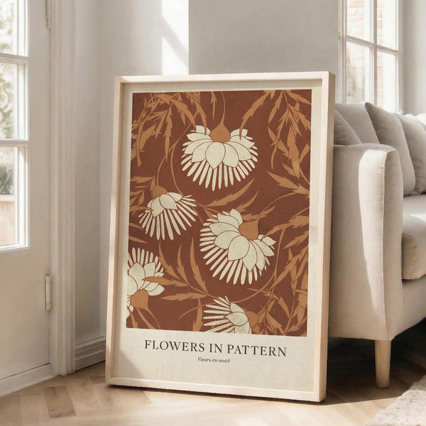 May include: Framed botanical art print leaning against white wall next to beige sofa in bright living room with large windows. The poster features stylized flowers and leaves in warm brown, cream and golden tones with text at bottom. Natural wood frame, approximately 2-3 feet tall, casting soft shadows on light wooden floor.