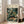 May include: Large framed art print leaning against white wall next to beige armchair in bright living room. Poster features tropical jungle scene with orange and black spotted wild cat resting among lush green palm fronds, exotic plants, and white flowers. Museum exhibition style design with cream background and black text header. Natural wood frame, approximately 24x36 inches based on room scale.