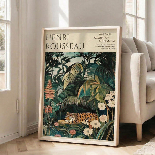 May include: Large framed art print leaning against white wall next to beige armchair in bright living room. Poster features tropical jungle scene with orange and black spotted wild cat resting among lush green palm fronds, exotic plants, and white flowers. Museum exhibition style design with cream background and black text header. Natural wood frame, approximately 24x36 inches based on room scale.