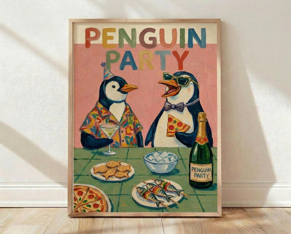 May include: Framed poster print leaning against white wall on light wooden floor. Artwork shows two cartoon penguins at party - one wearing colorful Hawaiian shirt and party hat holding martini glass, other in bow tie and sunglasses eating pizza slice. Pink background with multicolored "PENGUIN PARTY" text at top. Green table surface displays pizza, fish on plates, ice bowl, and champagne bottle. Natural wood frame, warm lighting with soft shadows.