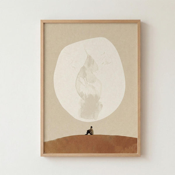 May include: Framed surreal art print showing a small figure sitting on a curved brown hill beneath a large pale moon on beige background, displayed in natural wood frame against white wall. Minimalist composition with earthy tones and dreamlike scale contrast between tiny person and oversized celestial body.