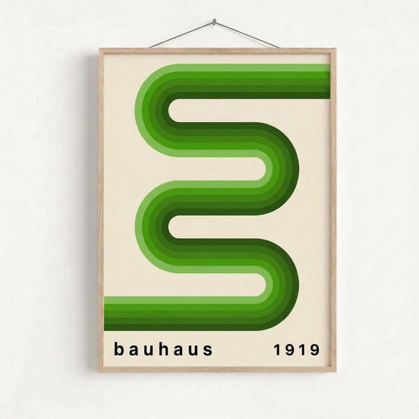 May include: Framed poster hanging on white wall showing green gradient serpentine ribbon design with multiple curved bands creating an S-like pattern. The artwork features layered green tones from light to dark on cream background, displayed in light wood frame with hanging wire. Text reads "bauhaus 1919" in black lowercase letters at bottom.