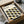 May include: Framed Bauhaus poster with geometric pattern of overlapping black and olive green oval shapes arranged in rows on cream background, being unpacked from cardboard shipping box with protective tissue paper wrapping on wooden surface