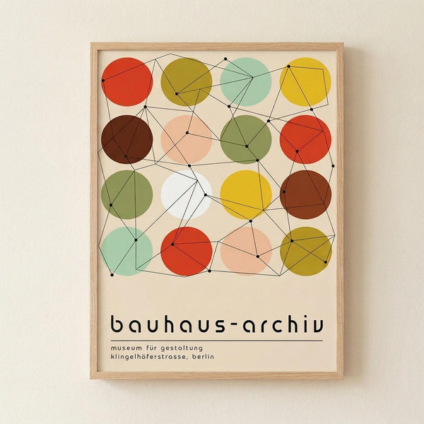 May include: Framed poster with colorful geometric design featuring overlapping circles in red, yellow, green, brown, and mint connected by black lines and dots, displayed on cream wall. Light wood frame surrounds cream background with "bauhaus-archiv" text and German museum details below the artwork.