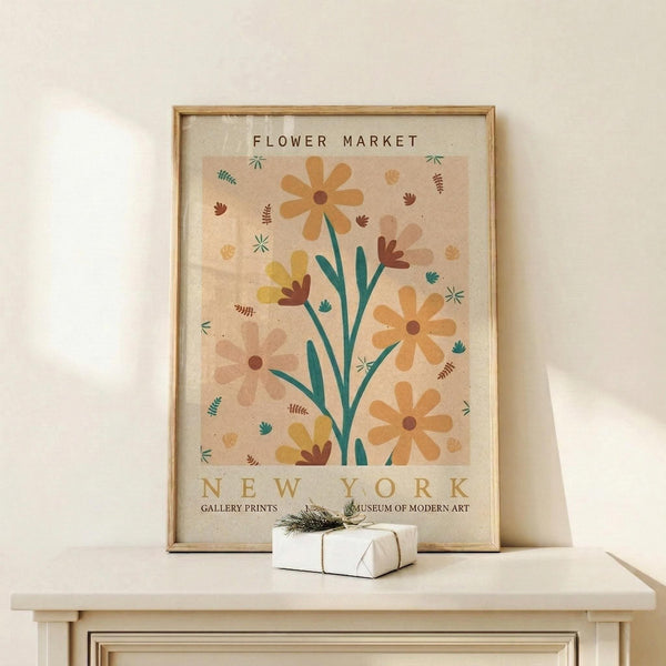 May include: Framed botanical poster with orange and yellow flowers on stems, surrounded by small leaves and botanical elements on a cream background, displayed in light wood frame on white wooden shelf next to small wrapped gift with twine and greenery sprig against neutral wall