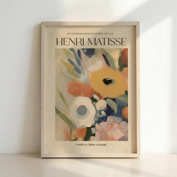 May include: Framed art print featuring abstract floral painting in soft watercolor style with yellow, coral, white and blue blooms against cream background. Text reads "Henri Matisse" at top and "creativity takes courage" at bottom. Light wood frame displayed on white surface against white wall with natural lighting creating gentle shadows.