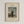 May include: Framed art print hanging on white wall showing Henri Rousseau's self-portrait painting from 1890. The artwork depicts a bearded man in black clothing holding a painter's palette, standing in a landscape with buildings, trees, and cloudy sky. The print has cream-colored matting with black text reading "MYSELF PORTRAIT LANDSCAPE" at top and "1890 FAMOUS PAINTING Henri Rousseau" at bottom, all within a light wood frame.