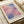 May include: Abstract art print with soft pink, purple, and blue watercolor-like rectangular color blocks in minimalist style, displayed in light wood frame on cream textured paper. Print sits on white bedding next to beige fabric, showing warm natural lighting and contemporary bedroom styling.