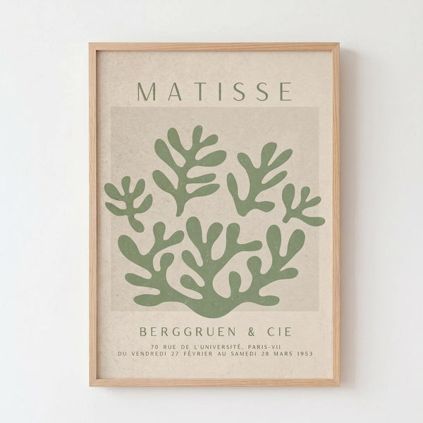 May include: Framed poster print with beige textured background featuring green coral-like organic shapes in Matisse's cut-out style. Text reads "MATISSE" at top and "BERGGRUEN & CIE" with French exhibition details at bottom. Light wood frame hangs on white wall.