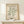 May include: Framed poster with cream background featuring sage green coral-like abstract cutout shape, displayed on light wood console table against white wall with small wrapped gift box beside it. Natural lighting creates soft shadows on the minimalist scene.
