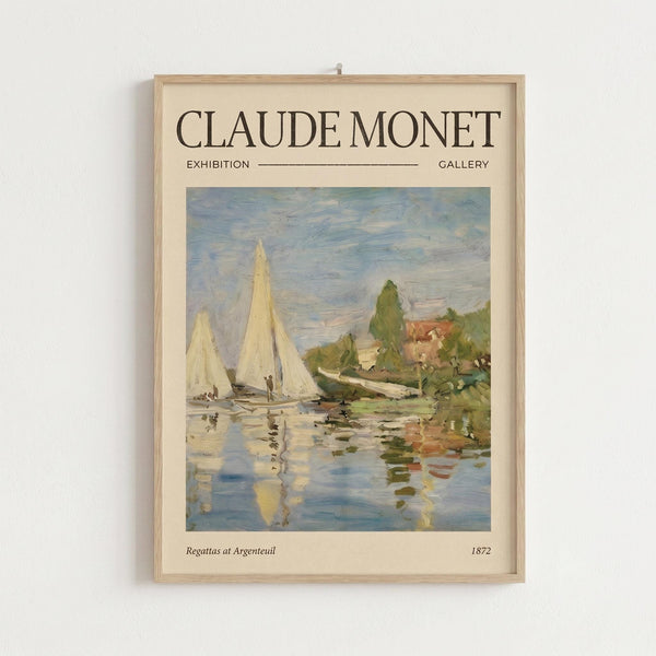 May include: Framed Claude Monet exhibition poster hanging on white wall, featuring sailboats on water with reflections in impressionist style. Light wood frame contains cream-colored poster with "CLAUDE MONET EXHIBITION GALLERY" text above painting of white-sailed boats near green shoreline under cloudy sky. Water shows blue and yellow reflections beneath vessels. Small text reads "Regattas at Argenteuil 1872" below artwork.