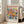May include: A framed poster featuring a vibrant floral bouquet in Matisse-inspired style with coral, yellow, and blue blooms against a cream background. The artwork displays "MATISSE" in bold red letters at the top and "06200 NICE, FRANCE" at the bottom. The light wood frame leans against a white wall next to a beige upholstered chair in a bright, naturally-lit room with white window frames.
