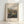 May include: Framed art print featuring an impressionist landscape painting with rolling hills, lush vegetation, and soft brushwork in greens, blues, and earth tones. The artwork shows a valley scene with mountains in the background under a cloudy sky. Displayed in a light wood frame against a white wall with natural lighting creating subtle shadows.