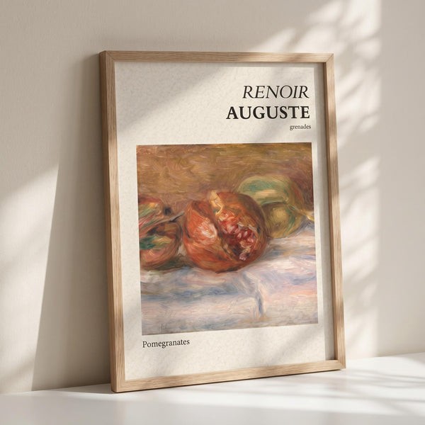 May include: Framed art print showing Renoir's impressionist painting of split pomegranates with ruby red seeds exposed, rendered in warm oranges and greens against soft brushstrokes. White matting displays "RENOIR AUGUSTE grenades" at top and "Pomegranates" at bottom in black text. Natural wood frame leans against white wall with window shadow patterns cast across the surface.