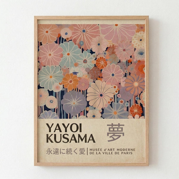 Framed poster featuring stylized flowers in soft pastels - pink, sage green, orange, and lavender blooms with radiating petal patterns against a dark background. Bottom section displays "YAYOI KUSAMA" in bold black text with Japanese characters and "永遠に続く愛 | MUSÉE d'ART MODERNE DE LA VILLE DE PARIS" on cream background. Light wood frame mounted on white wall.