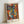 Abstract cubist-style artwork featuring fragmented faces with geometric shapes in vibrant blues, oranges, yellows, and greens. Multiple eyes, noses, and lips are arranged in overlapping angular forms reminiscent of Picasso's style. The print is displayed in a light wooden frame leaning against a white wall, with "PICASSO" and French text visible at the bottom of the poster.