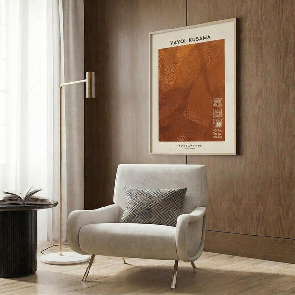 May include: Orange textured poster with dotted pattern and Japanese characters mounted on wood-paneled wall above cream upholstered armchair with geometric pillow. Modern reading nook features brass floor lamp, dark round side table with open book, and warm wood cabinetry. Poster displayed in light wooden frame against rich brown wood grain background.