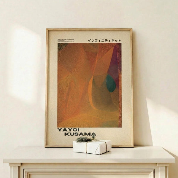 May include: Framed art print with abstract organic shapes in warm orange, rust, and burgundy tones with a teal accent, displayed on light wood surface next to small wrapped gift with evergreen sprig. Japanese text visible at top of cream-colored poster in natural wood frame against white wall.