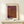 May include: Framed poster with Japanese text and textured purple-to-orange gradient pattern resembling organic cellular structures, displayed on light wood console table next to small wrapped gift with pine sprig, against cream wall in minimalist interior setting.