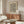 May include: Framed abstract art print featuring flowing black wavy lines on cream background, displayed above walnut wood credenza in minimalist living room with white textured chair, glass coffee table, and warm natural lighting creating shadows on beige walls.