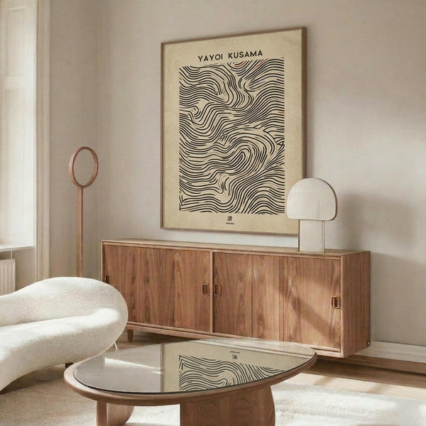 May include: Framed abstract art print featuring flowing black wavy lines on cream background, displayed above walnut wood credenza in minimalist living room with white textured chair, glass coffee table, and warm natural lighting creating shadows on beige walls.