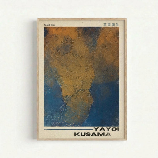 Framed art print featuring abstract organic forms in golden yellow and deep blue tones with distinctive dotted patterns throughout. The artwork shows flowing, cloud-like shapes created with small dots against a contrasting background. Text reads "Tokyo 1998" in upper left and Japanese characters in upper right, with "YAYOI KUSAMA" printed at bottom. The piece is displayed in a simple light wood frame against a white wall.