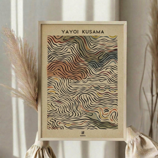 May include: Framed art print featuring flowing wave-like patterns in earth tones of brown, cream, orange and muted colors against a beige background, displayed on a light wooden surface beside dried pampas grass stems, with soft natural lighting and neutral fabric in a minimalist home setting.
