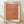 May include: Framed art print with light wood frame leaning against white wall on wooden floor. Poster features warm orange and coral gradient background with dotted mesh pattern overlay creating abstract geometric shapes. Japanese text at top, black text "YAYOI KUSAMA" at bottom on cream colored paper with white border.