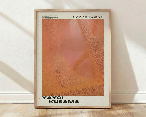 May include: Framed art print with light wood frame leaning against white wall on wooden floor. Poster features warm orange and coral gradient background with dotted mesh pattern overlay creating abstract geometric shapes. Japanese text at top, black text "YAYOI KUSAMA" at bottom on cream colored paper with white border.