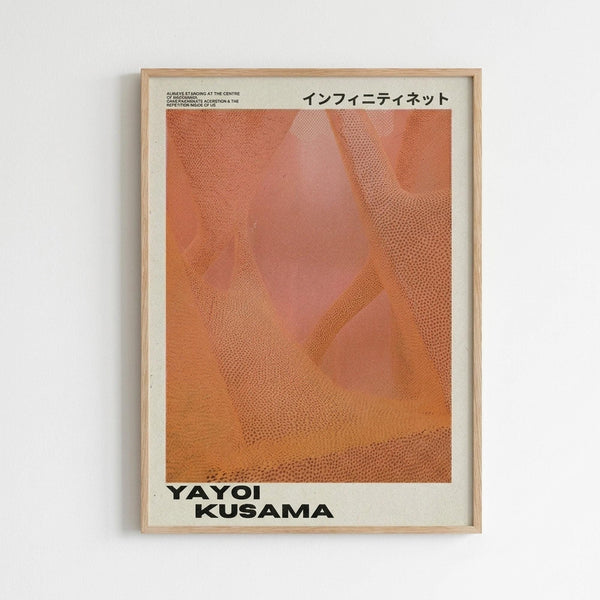 May include: Framed art print displayed on white wall featuring abstract orange and coral colored organic shapes with dotted texture patterns. Text at top reads "INFINITI NET" in Japanese characters, with "YAYOI KUSAMA" in bold black letters at bottom. Natural wood frame with white matting against minimalist interior setting.