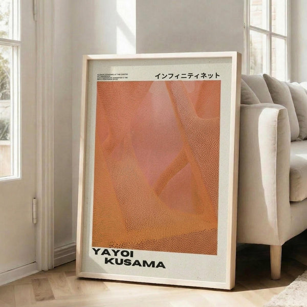 May include: Framed poster with orange and coral abstract dotted pattern leaning against white wall next to beige sofa in bright living room with large windows. Print features Japanese text at top, artist name at bottom, and textured halftone design creating flowing organic shapes in warm sunset tones within light wooden frame.