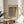 May include: Framed art print displayed on wooden side table next to beige upholstered chair and plant. Poster features abstract dotted pattern in muted browns and yellows with Japanese text, shown in natural wood frame against cream wall with soft window lighting.