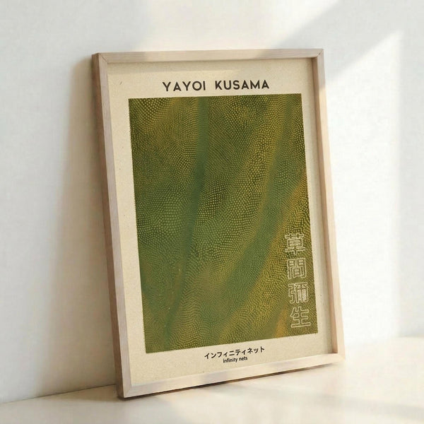 May include: Framed art print leaning against white wall showing green textured abstract pattern with small repeating dots creating flowing organic shapes. Light wooden frame surrounds cream-colored paper with black text at top and Japanese characters on right side. Natural lighting creates soft shadows on wall behind the rectangular vertical poster.