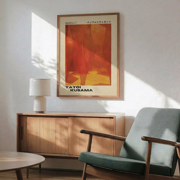 May include: Orange and yellow abstract art poster with Japanese text in wooden frame, displayed above mid-century modern wood credenza with white ceramic lamp. Mint green upholstered chair with wooden arms sits nearby on wooden floor. Warm sunlight creates geometric shadows on white wall in minimalist living room setting.