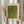 May include: Hands holding framed art print featuring green and yellow dotted pattern in Yayoi Kusama's infinity nets style, with Japanese text below the artwork. Light wooden frame with cream matting, held against neutral beige curtains with dried pampas grass visible on the left side.