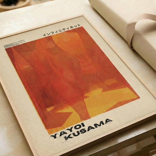May include: Orange and yellow abstract art print with dotted halftone texture displayed in white matted frame on cream colored surface. The artwork features warm gradient colors transitioning from deep red-orange at top to bright yellow at bottom, with Japanese text at the top and "YAYOI KUSAMA" printed at the bottom in black letters.