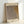 May include: Framed art print leaning against white wall showing abstract dotted pattern in muted browns and grays with Japanese text. Light wood frame with cream matting, captured in soft natural lighting that creates gentle shadows on the wall.