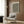 May include: Framed abstract art print with black wavy lines and yellow accents on cream background, displayed on wood paneled wall above beige upholstered chair with geometric patterned pillow. Modern reading corner features brass floor lamp and dark round side table with open book. Warm neutral tones throughout minimalist interior space.