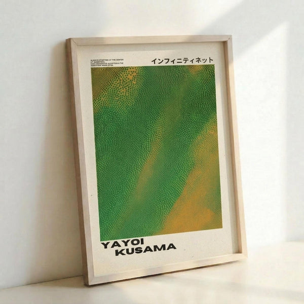 May include: A framed art print leaning against a white wall, featuring Yayoi Kusama's iconic polka dot pattern in vibrant green and yellow gradients. The artwork shows thousands of small dots creating flowing, organic shapes across the surface. Japanese text appears at the top, with the artist's name in bold black letters at the bottom. The print is displayed in a simple light wood frame on what appears to be a white surface.