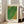 May include: Framed art print with green and yellow dotted pattern in light wood frame, leaning against white wall next to beige couch in bright living room with large windows. The poster features flowing organic shapes created from small dots that transition from bright green to golden yellow, with Japanese text at top and artist name at bottom.