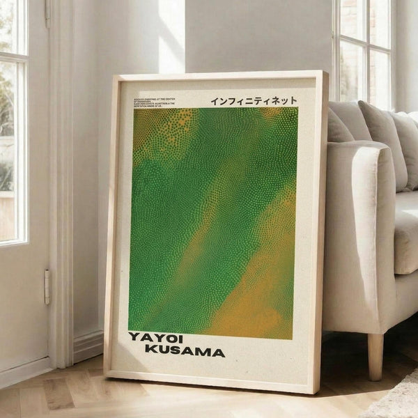May include: Framed art print with green and yellow dotted pattern in light wood frame, leaning against white wall next to beige couch in bright living room with large windows. The poster features flowing organic shapes created from small dots that transition from bright green to golden yellow, with Japanese text at top and artist name at bottom.