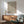 May include: Yayoi Kusama inspired poster with red polka dots creating optical illusion pattern on cream background, displayed in thin wooden frame above mid-century modern walnut credenza. Scene shows mint green upholstered armchair with wooden arms, small round coffee table, and white ceramic table lamp. Warm sunlight streams across white walls creating geometric shadows.