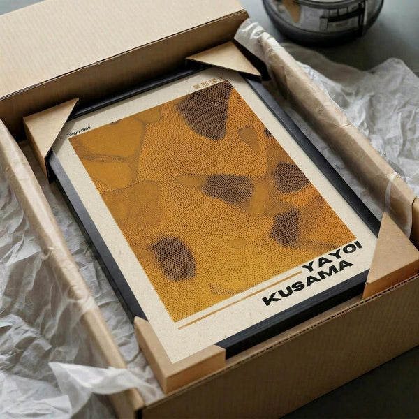 May include: Framed orange and brown abstract dotted art print displayed in wooden frame, surrounded by kraft paper packaging materials and white tissue paper in unboxing scene. Print features organic curved shapes created with halftone dot pattern technique in warm amber tones.