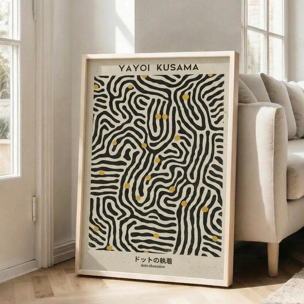 May include: Large framed poster with black and white organic flowing lines and small yellow dots, leaning against white wall beside beige sofa in bright living room with tall windows and natural light casting shadows on wooden floor.