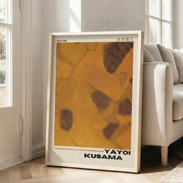 May include: Large framed poster with abstract orange and black dotted pattern reminiscent of Yayoi Kusama's signature polka dot style, displayed in bright modern living room with white walls, large windows, and beige sectional sofa on light wooden floors