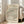 May include: Framed art print featuring flowing wavy lines in black, terracotta, and teal colors on cream background with Japanese character and "waves" text at bottom. Light wood frame leaning against white wall next to beige upholstered chair in bright room with large windows.