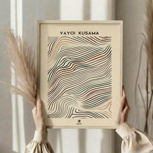 May include: Person holding framed abstract art print featuring flowing wave-like lines in black, terracotta, and sage green on cream background. Modern minimalist design with Japanese text. Light wood frame, neutral room setting with dried pampas grass and soft natural lighting.