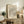May include: Framed art print with flowing black and terracotta wavy lines on cream background, displayed on rustic wooden sideboard alongside fern plant, ceramic vase, and stacked books in warm neutral living room setting