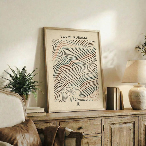 May include: Framed art print with flowing black and terracotta wavy lines on cream background, displayed on rustic wooden sideboard alongside fern plant, ceramic vase, and stacked books in warm neutral living room setting