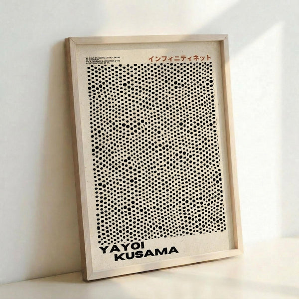 Framed poster featuring a pattern of black dots on white background that creates an optical illusion effect, with "YAYOI KUSAMA" text at bottom and Japanese characters at top. The artwork is displayed in a light wood frame leaning against a white wall, showing the distinctive polka dot infinity net pattern associated with contemporary art installations.